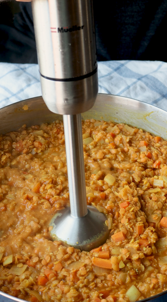 To make this creamy red lentil soup, begin by sautéing onions and minced garlic in oil. Then add carrots and seasonings. Cook for a few minutes, then add tomato paste, red lentils, and water. Bring to a boil, then cover and cook on super low for 30 minutes, or until lentils and carrots are soft. Blend until smooth, then add heavy cream. Add more heavy cream if a more soupy consistency is desired. Top with red pepper flakes and cilantro and enjoy!